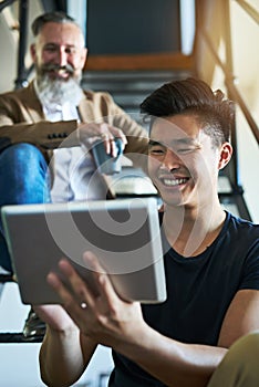 Its the smartest way to keep up with business. two businessmen using a digital tablet while sitting on a staircase in an