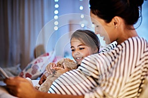 Its story time. an attractive young pregnant woman reading her daughter a bedtime story on a tablet.