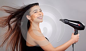 Its a straight hair kind of day. Studio portrait of an attractive young woman blowdrying her hair against a grey