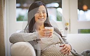 Its strictly decaf for a while. an attractive young pregnant woman drinking an iced coffee while relaxing on the sofa at