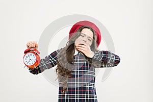 Its time to go to sleep. Sleepy little girl in evening time on yellow background. Yawning small child holding alarm