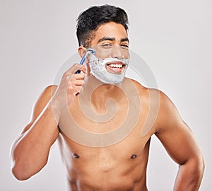 Its time for it to go. a young man shaving his beard against a grey background.