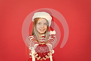 Its Xmas season. Happy child hold xmas tree ball. Little girl smile in xmas costume red background. Merry xmas to you