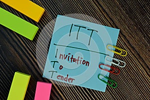 ITT - Invitation To Tender write on sticky notes isolated on Wooden Table
