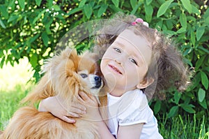 Ittle beautiful girl with pet on nature. happy child huging a dog. Female playing with Pomeranian Spitz outdoors. the best friends