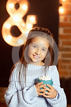 Ittle girl with a cup of cocoa. Girl in a sweater with a cup in her hands. Marshmellow on cocoa. Cozy photo