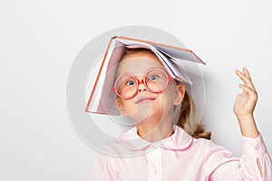 Ittle girl preschooler wearing glasses keeps an open book on her head