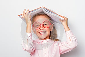 Ittle girl preschooler wearing glasses keeps an open book on her head