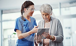 Ive got all the info right here. a young female nurse and her senior patient looking at a tablet in the old age home.