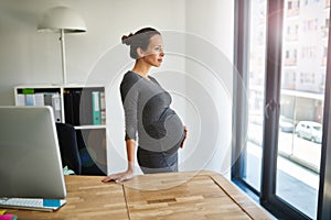 Ive got a future CEO right here with me...a pregnant businesswoman standing in her office holding her stomach.