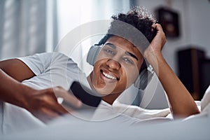 Ive got my quarantine entertainment covered. a young man using a smartphone and headphones while relaxing on his bed at