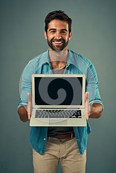 Ive got something exciting to show you. Studio portrait of a handsome young man holding a laptop with a blank screen