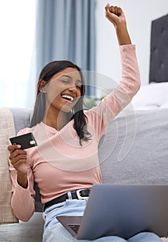 Ive just gotten the best deal. an attractive young woman cheering while holding a credit card and using her laptop in