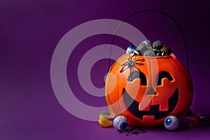 Jack-o-lantern bag full of candy on a purple background with copy space, horizontal