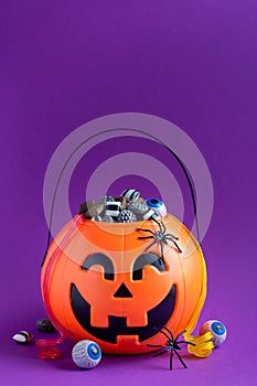 Jack-o-lantern bag full of candy on purple background with copy space,  vertical