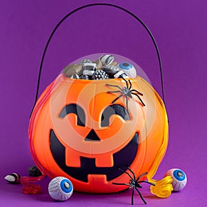 Jack-o-lantern bag full of candy on a purple background, square