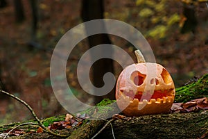 Jack O Lantern, with an evil face. Carved pumpkin for Halloween on fallen tree in night woods. Mysterious misty