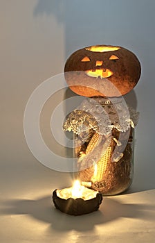 Jack o lantern on large glass jar of dried corn on the cob and corn silk. at the candle holder with a lighted candle