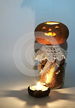 Jack o lantern on large glass jar of dried corn on the cob and corn stigmas. at the candle holder with a lighted candle