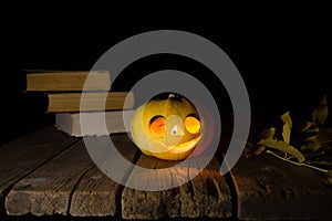 Jack O`Lantern. A pumpkin with burning eyes. A pumpkin for Halloween on an old wooden table against the background of old books.