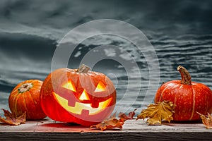 Jack o lanterns Halloween pumpkin face on wooden background and autumn leafs