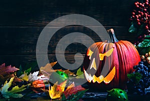 Jack o lanterns Halloween pumpkin face on wooden background and autumn leafs photo