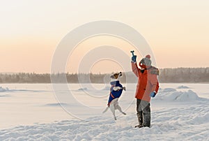 Kid in warm winter outfit playing in snow with dog on beautiful brumal day photo