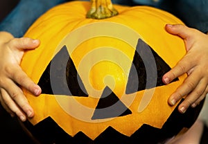 Jack's pumpkin head for Halloween in the blurry hands of a child. A little girl holds a big terrible pumpkin close-up.