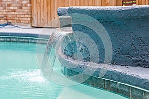 A jacuzzi hot tub next to a large freeform swimming pool with a waterfall water feature running