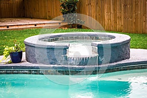 A jacuzzi hot tub next to a large freeform swimming pool with a waterfall water feature running