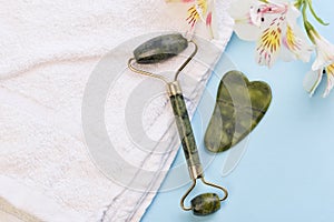 Jade roller for face massage. Green gua sha facial massager tools. Anti age, lifting and toning treatment on a white towel