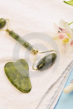 Jade roller for face massage. Green gua sha facial massager tools. Anti age, lifting and toning treatment on a white towel