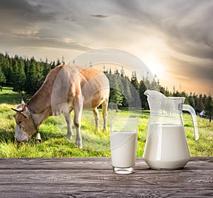 Jag and glass of milk against background of cow and mountain pas