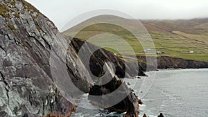 Jagged coastal rocks and tall steep cliffs along sea coast. Countryside with green meadows and pastures. Ireland