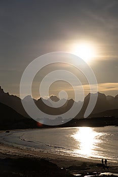 The jagged mountains and skyline of Lofoten with a low sun reflecting in the sea, Norway