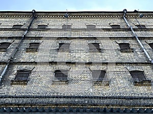 Jail. Antique prison wall with barred windows and barbed wire