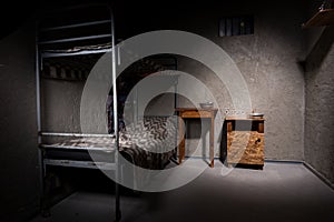 Jail cell with iron bunk bed and wooden bedside table