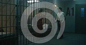 Jailer with police baton stands near prison cell photo