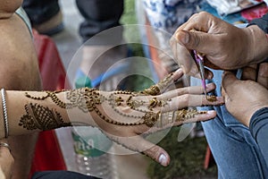 Jaipur, India. march 27 2023 A henna artist drawing a peacock design henna tattoo on a womanâ€™s forearm, hand and fingers