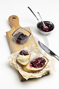 Jam in glass bowl, loaf slices with butter and jam on cutting board