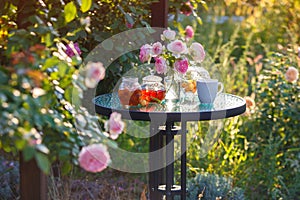 Jam in glass jar. Romantic dinner in the garden under a rose bush.