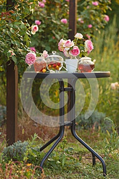 Jam in glass jar. Romantic dinner in the garden under a rose bush. Summer time. Vertical frame