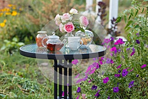 Jam in glass jar. Romantic dinner in the garden under a rose bush.