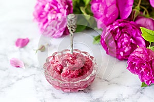 Jam with rose petals in a glass bowl and bright roses on a light background.