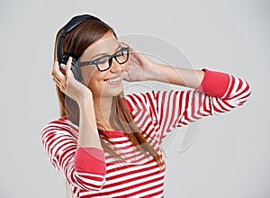 Jammin to my tunes. Studio shot of an attractive young woman listening to music on headphones on a grey background.