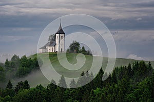 Jamnik church on a hillside in the spring, foggy weather at sunset in Slovenia, Europe. Mountain landscape shortly after spring ra