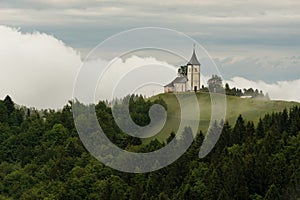 Jamnik church on a hillside in the spring, foggy weather at sunset in Slovenia, Europe. Mountain landscape shortly after spring ra