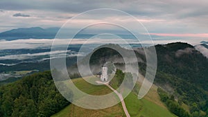 Jamnik, Slovenia - Aerial time-lapse hyperlapse footage of drone flying by St Primoz church on a foggy summer morning