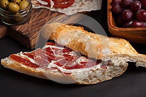 Jamon Iberico with white bread, olives on toothpicks and fruit on a dark background photo
