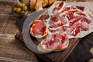 Jamon Iberico with white bread, olives on toothpicks and fruit on a wooden background. Top view photo